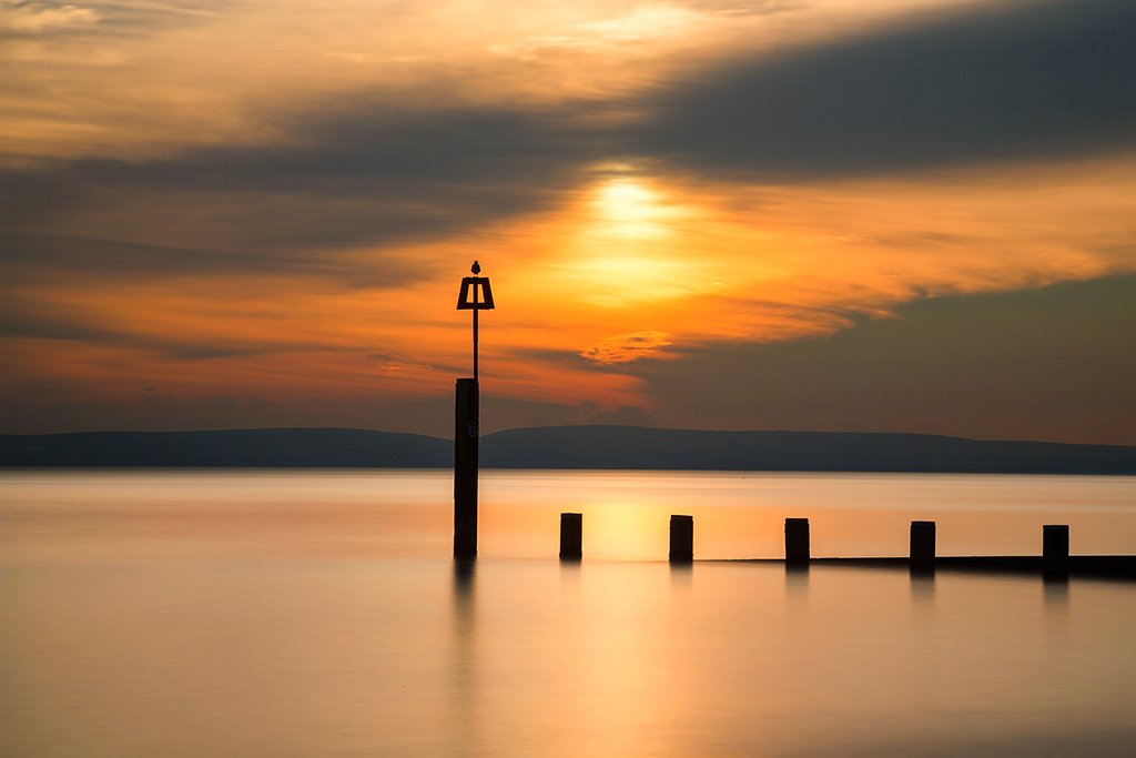 Seascape long exposure at sunset of wooden groyne and ocean sea with fence and seagull bird Seascape long exposure at sunset of wooden groyne and ocean sea with fence and seagull bird
