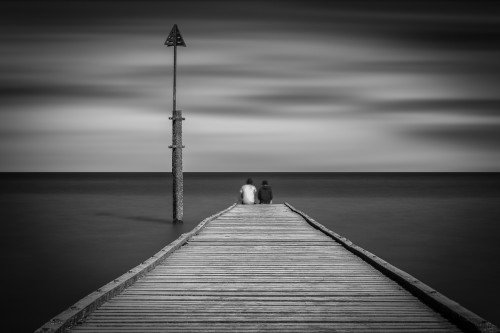 friends sitting at end of board ward long exposure at the ocean